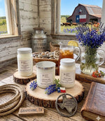 Load image into Gallery viewer, Three hand poured Candles on wooden stands with a rustic setting featuring a barn and outdoor scene. Southern Charm Farmhouse.