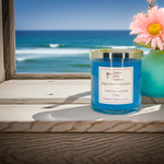 Load image into Gallery viewer, 2 Wick hand poured Blue candle labeled 'Baja Cactus Blossom' on a wooden surface with ocean view. Southern Charm Farmhouse.