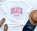 Load image into Gallery viewer, White t-shirt with 'BEACH BABE' text, brown hat, denim shorts, and sandals on a light background. Southern Charm Farmhouse.