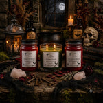Load image into Gallery viewer, Three gothic-themed hand-poured candles displayed on a rustic wooden surface with a dark, atmospheric Halloween background featuring a skull, lantern, potion bottles, and books. The candles include a red wax 'Dragon's Blood' candle, a green wax 'Poison Apple' candle, and a red wax 'Vampire's Blood' candle. Southern Charm Farmhouse