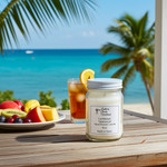Load image into Gallery viewer, Hand poured Caribbean Teakwood Candle on a table with fruit and iced tea, set against a tropical beach backdrop. Southern Charm Farmhouse.
