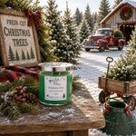 Load image into Gallery viewer, A green jar hand poured candle with a silver lid sits on a rustic wooden table in a snowy Christmas outdoor scene. The label reads 'Christmas Tree' and 'Made in Texas. Southern Charm Farmhouse.