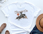 Load image into Gallery viewer, White t-shirt with 'Cowgirl On' graphic design featuring a cowgirl riding a horse, placed on a light surface with a hat and boots. Southern Charm Farmhouse.