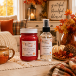 Load image into Gallery viewer, Two home fragrance products from Southern Charm Farmhouse displayed on a table runner in a cozy autumn-themed setting: an Apple Berry Harvest hand-poured candle in a red jar and a Muted Cider Pear Room Spray in a clear bottle.