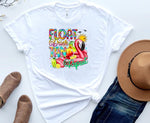 Load image into Gallery viewer, A white t-shirt with a colorful graphic that reads 'FLOAT DRINK TAN REPEAT' accompanied by an image of a pink flamingo and ice cream cones, displayed on a flat surface with a pair of blue jeans, brown hat, and brown shoes. Southern Charm Farmhouse.