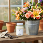 Load image into Gallery viewer, 16 oz mason jar of French Market Candle, flowers in a metal bucket, and gardening tools on a wooden table. Southern Charm Farmhouse