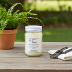 Load image into Gallery viewer, Hand poured Green Clover & Aloe candle in a 16 oz Mason jar with a label, placed on a wooden surface with a plant and tools in the background. Southern Charm Farmhouse