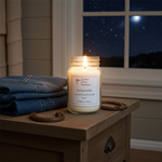 Load image into Gallery viewer, A lit Gunpowder hand-poured candle in a Mason jar, glowing on a wooden nightstand. Next to the candle is a stack of folded denim and two rustic iron horseshoes. In the background, a window looks out onto a dark, starry night sky with a bright moon. Southern Charm Farmhouse.