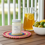Load image into Gallery viewer, Jamaica Me Crazy Candle in a 16 oz. Mason Jar on a colorful coaster with a pitcher of lemonade and fruit bowl on a wooden table. Southern Charm Farmhouse.