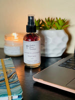 Load image into Gallery viewer, A 4 oz bottle of Spring/Summer room spray with a black spray nozzle, labeled with the product name and brand. The bottle is on a wooden surface, accompanied by a lit candle, a plant, and a laptop, creating a cozy ambiance. Southern Charm Farmhouse.