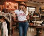 Load image into Gallery viewer, Girl standing in a Western Style in a t shirt that reds Long Live Cowgirls. Western apparel and purses around her. Southern Charm Farmhouse.