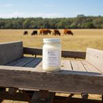 Load image into Gallery viewer, 16 oz Mason Jar of 'Open Range' hand poured candle on a wooden surface with a field and cows in the background. Southern Charm Farmhouse.