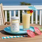 Load image into Gallery viewer, 16 oz Mason jar hand poured Pina Colada candle sitting on a blue tray with a drink and umbrella in it and the ocean behind it. Southern Charm Farmhouse.