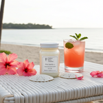Load image into Gallery viewer, Pink Sands Candle in a 16 oz Mason jar with a cocktail on a beach setting with flowers and shells. Southern Charm Farmhouse.