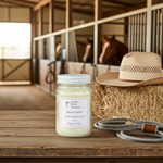 Load image into Gallery viewer, Ranch Hand Candle in a 16 oz. Mason jar with a cowboy hat and lasso on a wooden surface, horse stable in the background. Southern Charm Farmhouse.