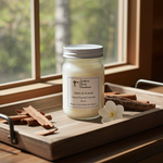 Load image into Gallery viewer, 16 oz hand poured jar of Satin & Suede candle on a wooden tray with cinnamon sticks and a flower, in front of a window. Southern Charm Farmhouse.