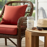 Load image into Gallery viewer, 16 oz mason jar hand poured Scarlet Sunset Candle on a wooden table next to a wicker chair with red cushions and a straw hat. Southern Charm Farmhouse.
