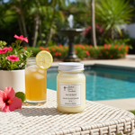 Load image into Gallery viewer, 16 oz Mason Jar of Sun & Sand hand poured candle and glass of lemonade on a table by a pool with flowers and a fountain in the background. Southern Charm Farmhouse.