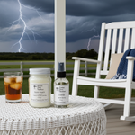 Load image into Gallery viewer, Outdoor setting with a stormy sky, white rocking chair, and One 16 oz hand poured mason jar Storm Watch candle and one 4 oz Leather Room Spray on a table. Southern Charm Farmhouse.