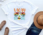 Load image into Gallery viewer, A white t-shirt with a 'Vacay Mode' graphic design featuring a tropical pineapple motif, displayed with a pair of blue jeans, a hat, and a pair of sandals. Southern Charm Farmhouse.