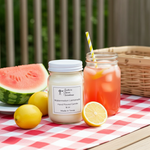 Load image into Gallery viewer, Watermelon Lemonade Candle in a 16 oz. Mason Jar on a checkered tablecloth with a drink and fruit. Southern Charm Farmhouse.