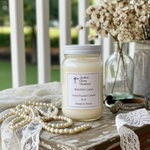 Load image into Gallery viewer, Hand poured 16 oz mason jar Western Lace candle with label on a wooden farmhouse porch outdoors, with pearls, flowers and a bracelet by it. Southern Charm Farmhouse.