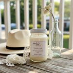 Load image into Gallery viewer, Hand poured 16 oz mason jar candle labeled 'Western Lace' on a wooden surface with a hat and bottle in the background. Southern Charm Farmhouse.