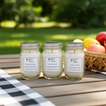 Load image into Gallery viewer, Three hand poured 4 oz candles in glass jars with metal lids on a wooden table outdoors. Southern Charm Farmhouse.