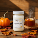 Load image into Gallery viewer, 16 oz mason Jar of Vanilla Maple Pecan hand poured candle with a pumpkin and steaming mug in the background on a wooden surface. Southern Charm Farmhouse.