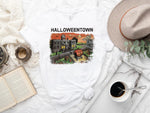 Load image into Gallery viewer, A white unisex t-shirt with 'Halloweentown' text and a graphic print featuring a cartoonish depiction of a town and its inhabitants on the front. Southern Charm Farmhouse.