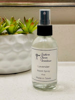 Load image into Gallery viewer, A clear 4 oz. spray bottle labeled 'Lavender Room Spray' made with water, hazel witch, and fragrance oil, placed on a countertop with a plant in the background. Southern Charm Farmhouse.
