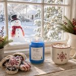 Load image into Gallery viewer, A blue hand poured candle labeled 'Jack Frost' sits on a wooden windowsill next to a white mug filled with marshmallows and hot chocolate, with cozy knit mittens and winter greenery nearby. Through the window, a snowman in a black top hat is visible outside in a snowy yard.  Southern Charm Farmhouse.
