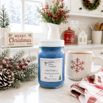 Load image into Gallery viewer, A blue wax candle in a clear glass jar with a white lid and a white label reading 'Southern Charm Farmhouse - Jack Frost scent' is styled on a kitchen counter next to a white mug with a red snowflake, holiday greenery, and a 'Merry Christmas' sign.
