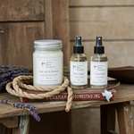 Load image into Gallery viewer, 1 16 oz Hand poured Mason jar candle with 2 Room Spray bottles of scented products on a wooden surface with lavender and a book in the background. Southern Charm Farmhouse.
