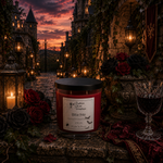 Load image into Gallery viewer, A red wax hand poured candle in a clear glass jar with a black lid sits on a stone surface in a moody gothic courtyard at sunset. The label reads Bite Me Hand Poured 2 Wick. Southern Charm Farmhousee.
