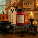 Load image into Gallery viewer, A red wax hand poured candle in a 16 oz mason jar with a black lid and a label reading ' Bite Me ' is styled on a wooden table with Halloween props including a black cauldron, old books, a white ghost figurine, a lit candle, a spider decoration, and a 'Trick or Treat' sign. Southern Charm Farmhouse.
