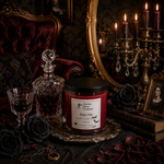 Load image into Gallery viewer, A gothic-themed candle jar labeled 'Bite Me' by Southern Charm Farmhouse, styled on a silver tray with a glass decanter, goblet, black roses, a gold candelabra, and a dark velvet chair in the background.
