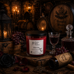 Load image into Gallery viewer, A red wax candle in a clear glass jar with a black lid and a white label reading 'Bite Me' and 'Southern Charm Farmhouse.,' styled on a rustic wooden surface with wine bottles, grapes, a glass, lanterns, and a dark gothic background.
