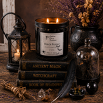 Load image into Gallery viewer, A black glass jar candle labeled 'Black Magic' sits on stacked gothic books, surrounded by a lantern, dried flowers, a glass cloche, a feather quill, and small ritual props on a rustic wooden surface. Southern Charm Farmhouse.
