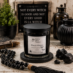 Load image into Gallery viewer, A black wax hand poured candle in a clear glass jar with a black lid sits on a round black coaster on a rustic white wood table. The label reads 'Southern Charm Farmhouse' and 'Black Magic'.
