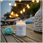 Load image into Gallery viewer, 16 oz Mason jar hand poured Black Sea Candle with a label on a wooden surface near a body of water with string lights. Southern Charm Farmhouse
