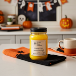 Load image into Gallery viewer, 16 oz mason jar Yellow hand poured candle labeled 'Candy Corn' on a black napkin with Halloween decorations in the background. Southern Charm Farmhouse

