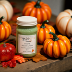 Load image into Gallery viewer, A hand-poured candle in a clear 16 oz mason jar with a white lid sits on a rustic wooden surface surrounded by decorative pumpkins and autumn leaves. The candle wax is a muted sage green, and the label reads ' Cedar &amp; Autumn Leaves'.  Southern Charm Farmhouse.

