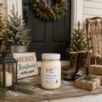 Load image into Gallery viewer, A 16 oz mason jar hand poured candle labeled 'Christmas Cheer ' sits on a rustic wooden porch doormat, surrounded by holiday decorations including a lantern, 'Merry Christmas' sign, wreath, wrapped gifts, and winter boots. Southern Charm Farmhouse.

