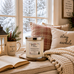 Load image into Gallery viewer, A holiday-themed hand poured scented candle labeled Christmas Cheer in a glass jar sits on a wooden tray on a cozy windowsill. The candle is surrounded by seasonal props including a mug, a lantern, an open book, and a knitted throw blanket. Southern Charm Farmhouse.
