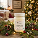 Load image into Gallery viewer, A hand-poured candle in a clear16 oz mason jar with a white lid sits on a wooden table surrounded by pine branches, pinecones, and red berries, with a decorated Christmas tree and cozy living room in the background. The label reads 'Christmas Cheer'. Southern Charm Farmhouse.
