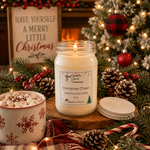 Load image into Gallery viewer, A lit white hand poured candle in a clear 16 oz mason jar sits on a wooden board surrounded by Christmas decorations, including pine branches, red berries, pinecones, a mug of whipped cream and marshmallows, and a sign that reads 'HAVE YOURSELF A MERRY LITTLE Christmas'. The candle label shows the name of the candle as Christmas Cheer by Southern Charm Farmhouse.
