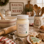 Load image into Gallery viewer, A 16 oz mason jar candle labeled 'Christmas Cheer Hand Poured Candle' sits on a rustic kitchen counter surrounded by baking props like a rolling pin, cookie cutters, decorated cookies, eggs, and a mug with wooden utensils. Southern Charm Farmhouse.
