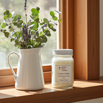 Load image into Gallery viewer, Coastal Cottage Candle in a 16 oz. Mason jar with a pitcher of plants on a windowsill and sunshine coming in. Southern Charm Farmhouse.
