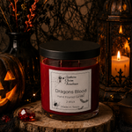 Load image into Gallery viewer, A red  scented hand poured candle in a clear glass jar with a black lid sits on a rustic wood slice. The label reads 'Southern Charm Farmhouse' and 'Dragons Blood'.
